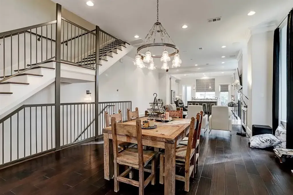 Dining room with wooden table and chairs, staircase, chandelier, and hardwood floors.