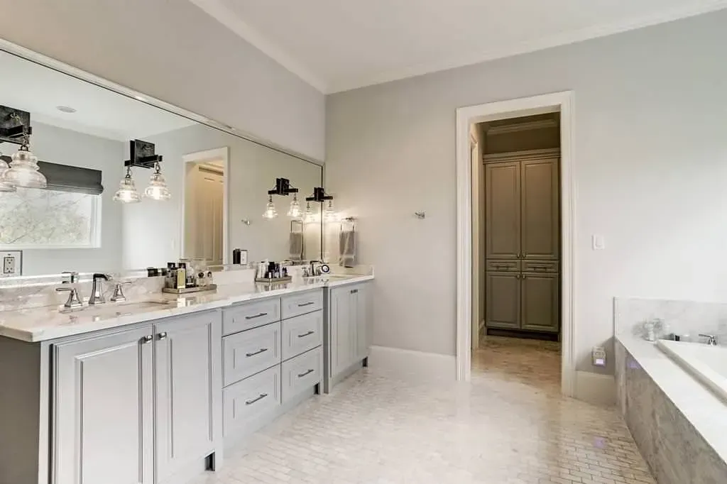 Gray bathroom with double vanity, large mirror, and open door to closet.