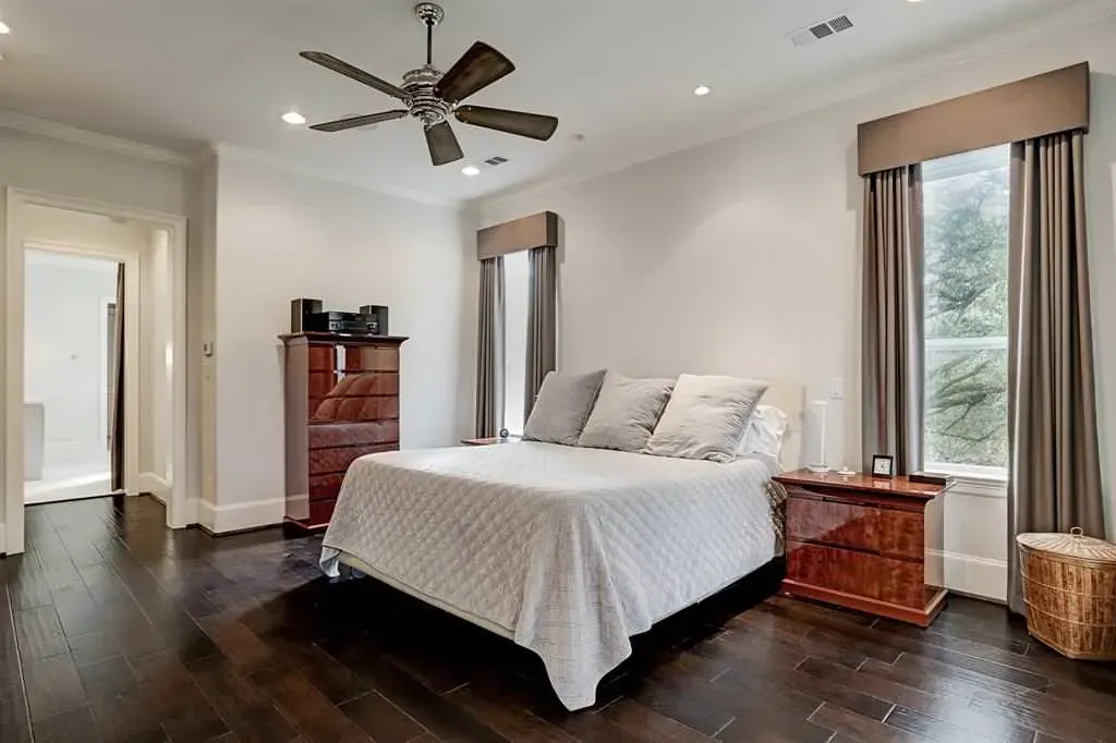 Bedroom with bed, dark wood floor, and two windows with curtains. A ceiling fan is visible.