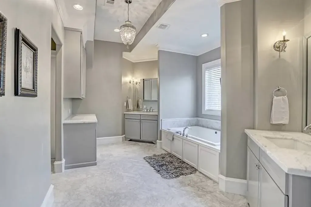 Spacious gray and white bathroom with a soaking tub, double sinks, and a chandelier.