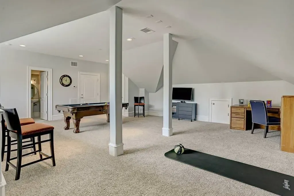 Spacious room with pool table, desk, and TV; carpeted floor and sloped ceiling.