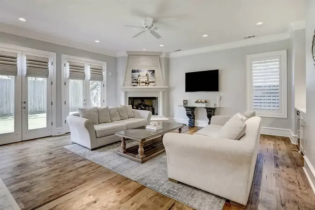 Living room with white sofas, fireplace, and hardwood floors.