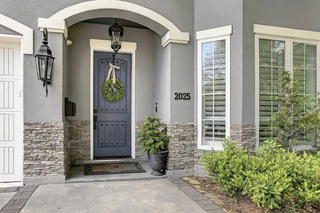 Gray house front door with stone accents, wreath, and potted plant.