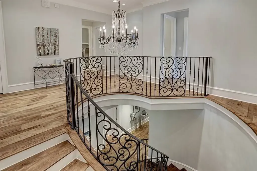 Grand foyer with curved staircase, wrought iron railing, chandelier, and hardwood floors.