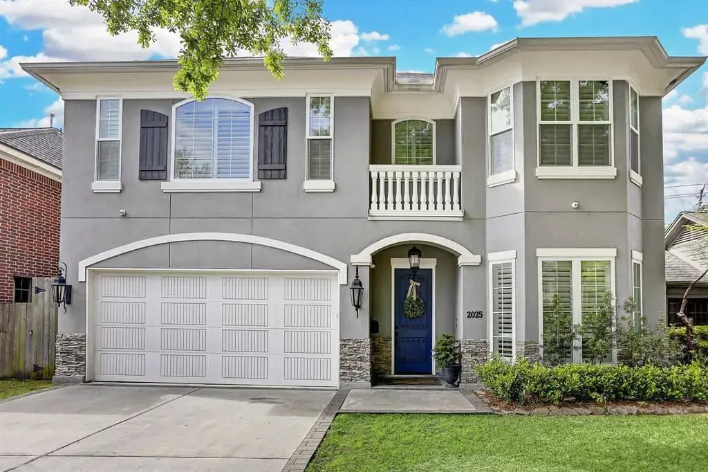 Two-story gray stucco house with a blue front door, white garage door, and green lawn.