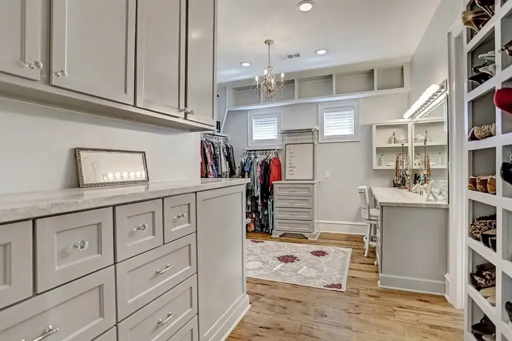Spacious walk-in closet with gray cabinetry, clothes, and shoe shelves; light-colored rug and flooring.