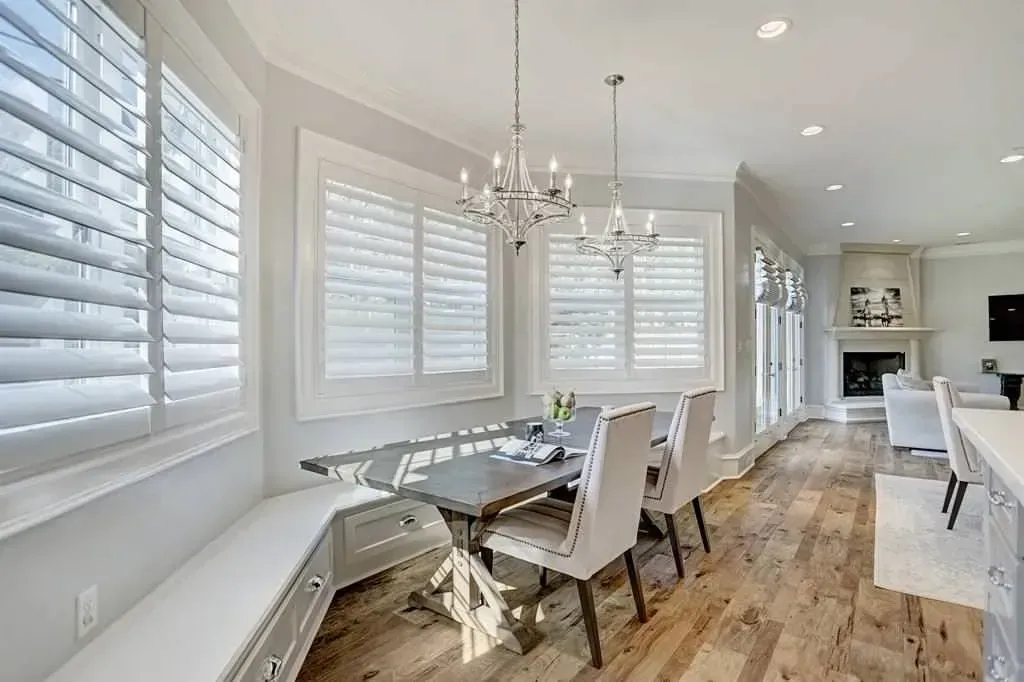 Dining room with a table, chairs, bench seating, and chandelier. Wooden floor, windows with shutters.