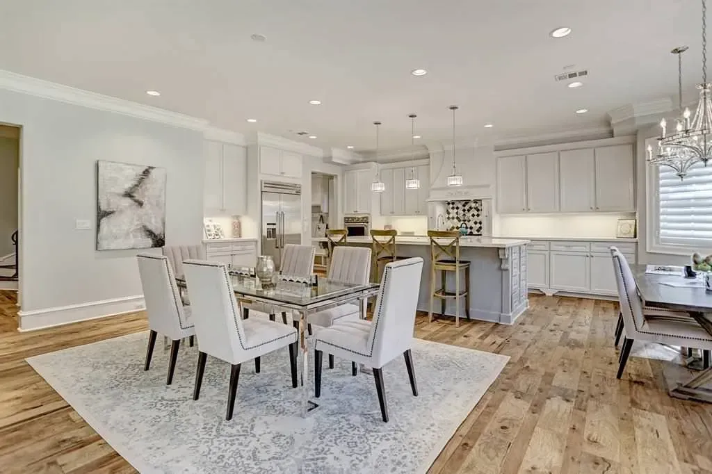 Kitchen and dining area with white cabinets, light wood floors, and a dining table with six upholstered chairs.