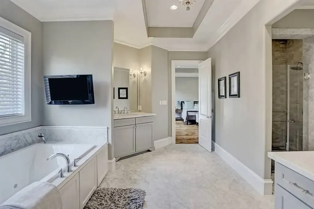 Luxury bathroom with a jacuzzi, cabinets, a mounted TV, and an open doorway.