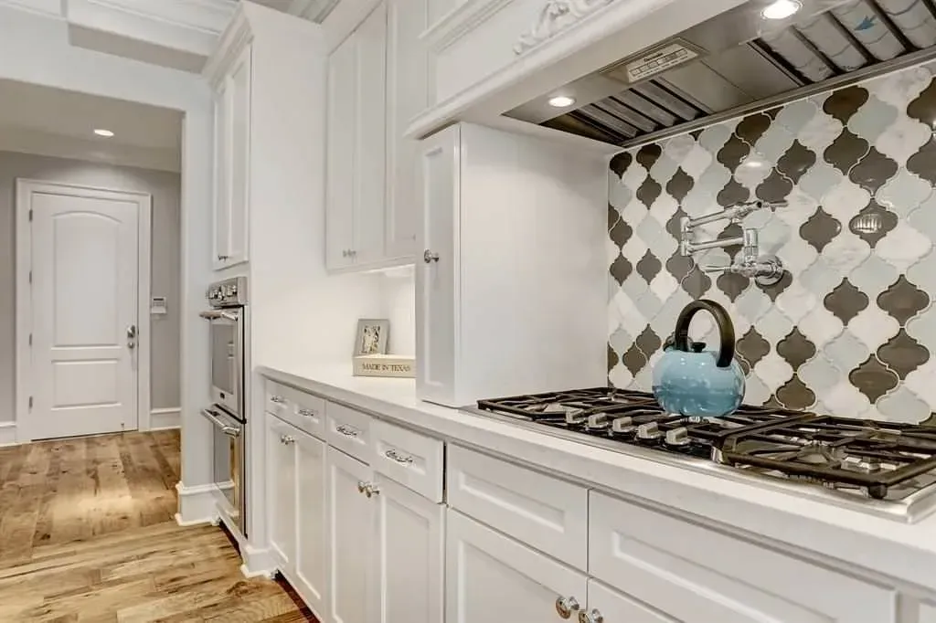 White kitchen with gas range, patterned tile backsplash, and blue kettle.