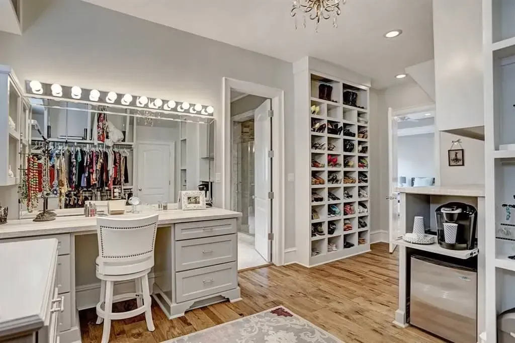 Walk-in closet with vanity, shoe shelves, and refrigerator in a light-filled room.