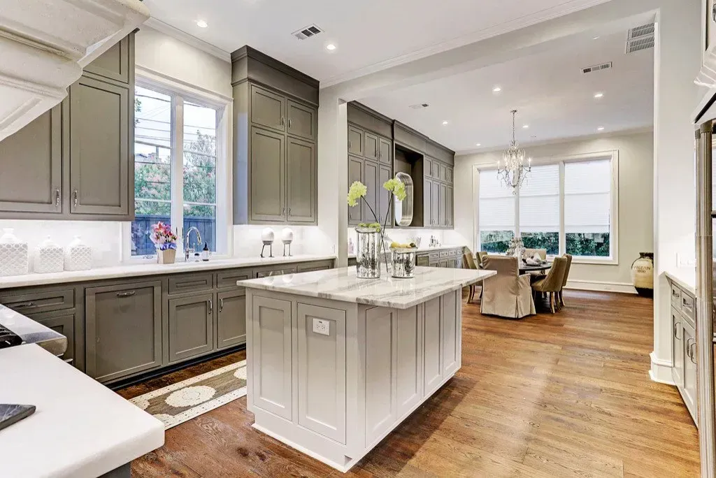 Gray kitchen with island, marble countertops, and hardwood floors. Dining area visible.