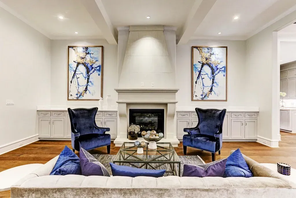 Living room with fireplace, blue armchairs, abstract art, and a light-colored couch.