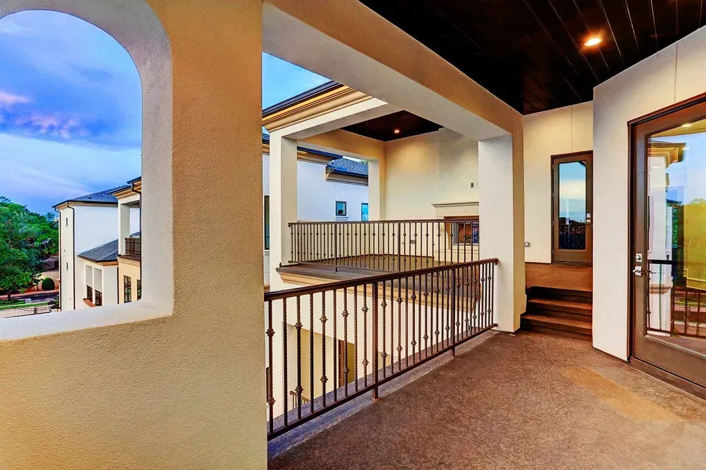 Balcony with railing overlooking an exterior with a building and sky view through an arched window.