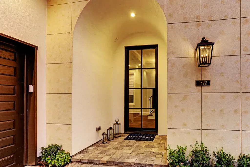 Exterior arched entryway with a black door, sidelight, lantern, and beige stone walls.