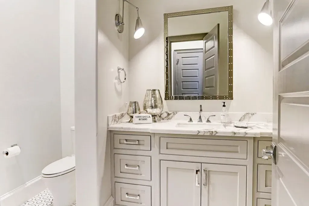 Bathroom with light gray cabinets, marble countertop, and a mirror.