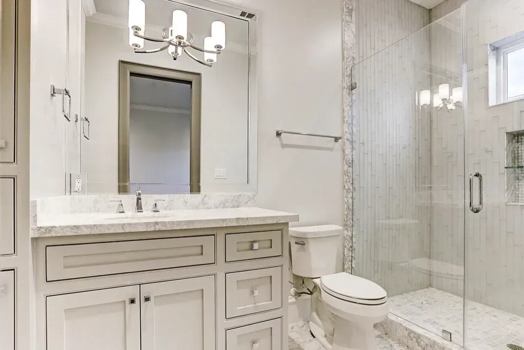 Bathroom with white vanity, shower, and toilet; gray and white tile walls and floor.