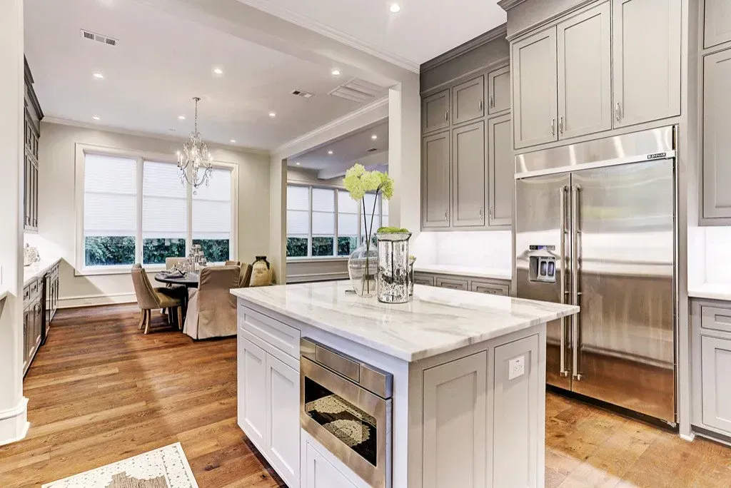 Kitchen with white marble island, stainless steel refrigerator, and gray cabinets. Dining area visible.