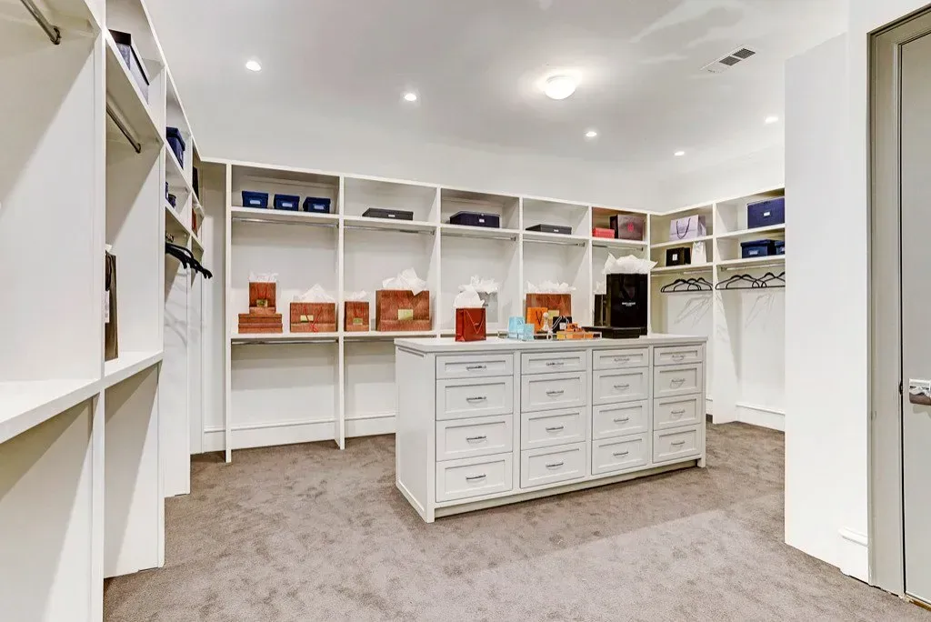 Walk-in closet with white shelves and drawers, displaying items. Gray carpeted floor.