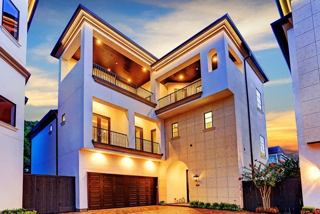 Multi-story modern home with balconies and a wooden garage door at dusk.