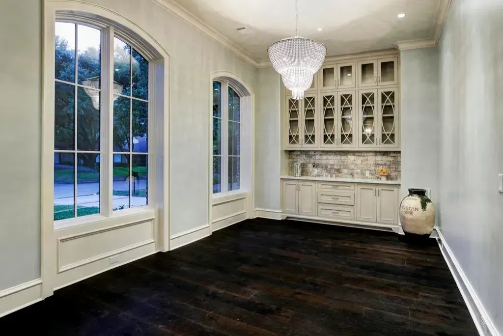 Elegant room with dark wood floors, built-in cabinet, large windows, and a chandelier.