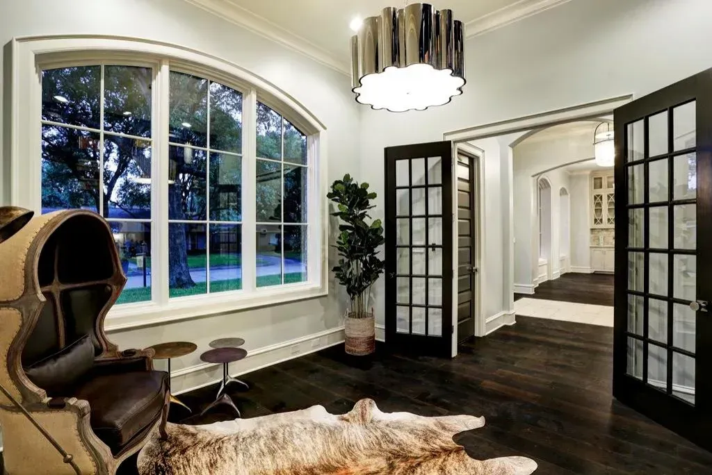 Interior room with large arched window, dark wood floors, decorative light fixture, and leather chair.