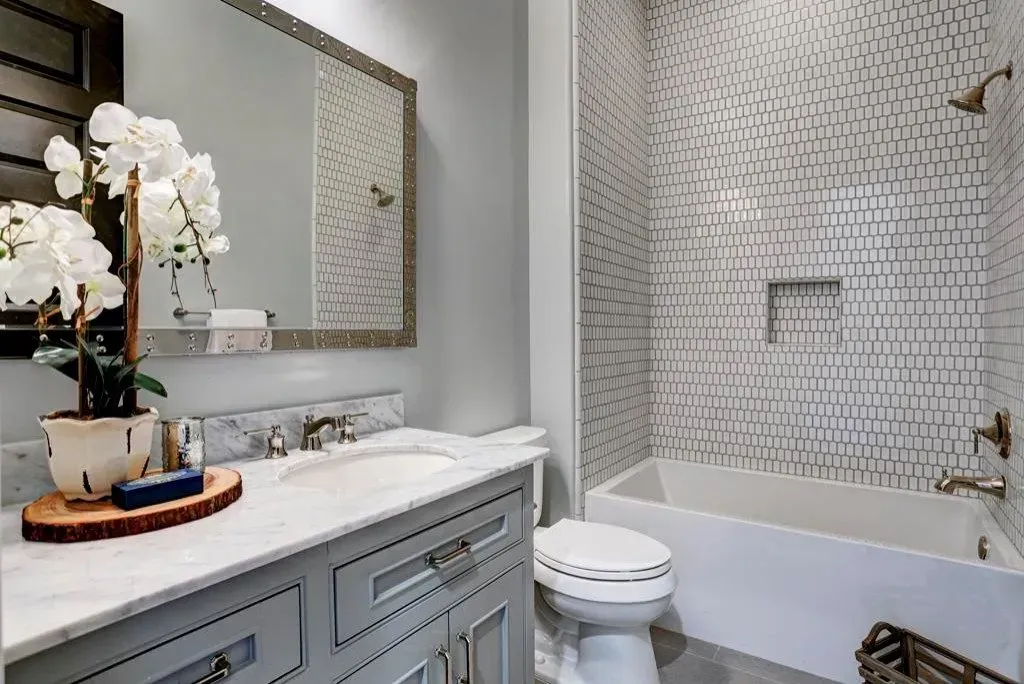 Bathroom with gray vanity, white marble countertop, bathtub with tile surround, and orchid.