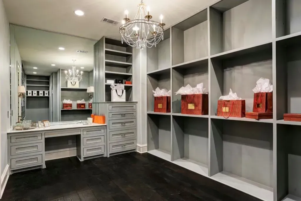 Gray walk-in closet with shelves, drawers, vanity, dark floor, and chandelier.