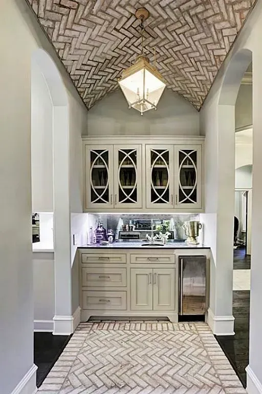 Hallway with wet bar: brick ceiling, light cabinetry, mirrored backsplash, under-cabinet lighting.