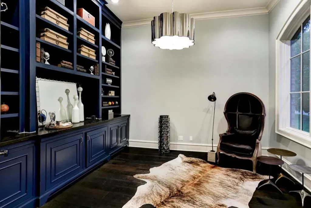 Navy blue home office with built-in shelves, cowhide rug, chair, and decorative lighting.