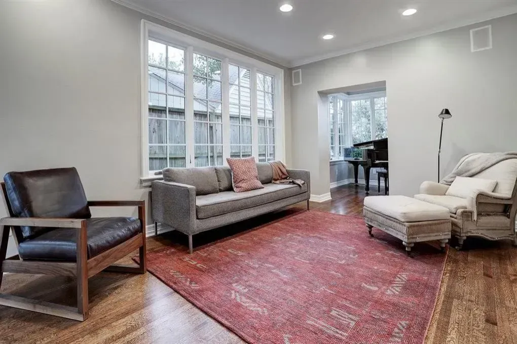 Living room with gray sofa, red rug, leather chair, and large window.