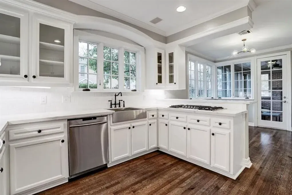 White kitchen with wood floors; stainless steel appliances; cabinets; large windows.