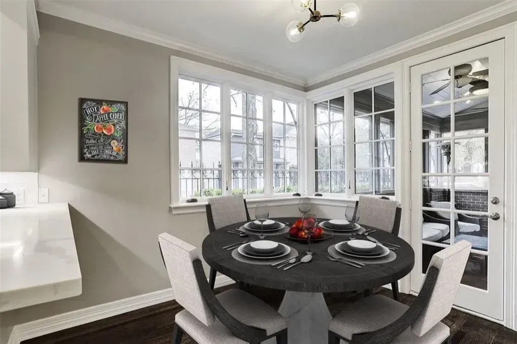 Dining room with round table, chairs, and large windows.  Gray walls, dark table, white trim, and a small framed picture.