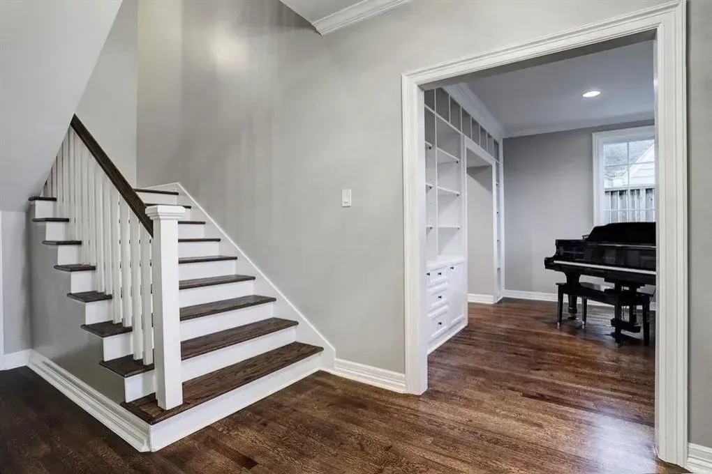 Staircase with white railing and dark wood steps, leading to a room with a piano and built-in shelves.