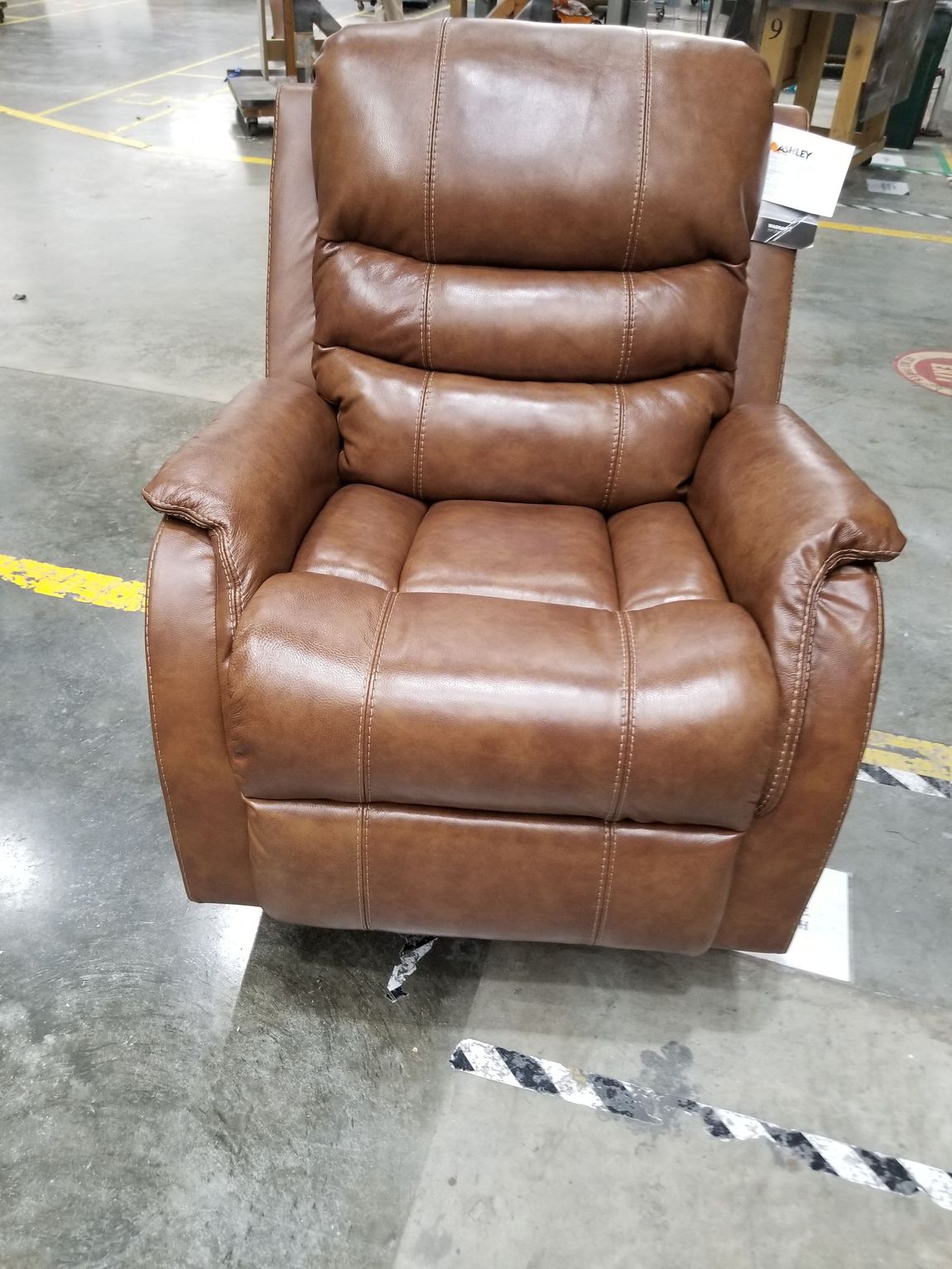 A brown leather recliner is sitting on a concrete floor in a warehouse.