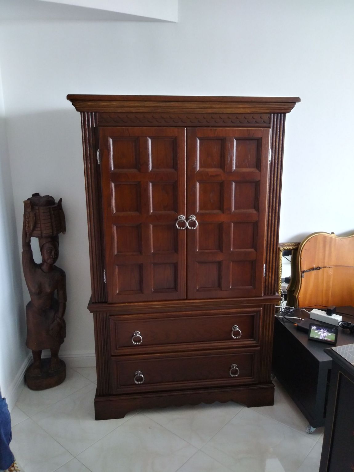 A large wooden cabinet is in a living room next to a statue