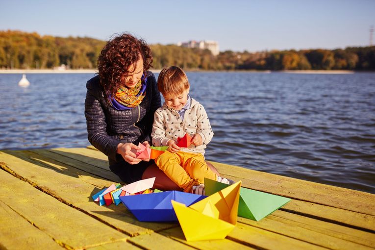 A woman and a child are sitting on a dock playing with paper boats.