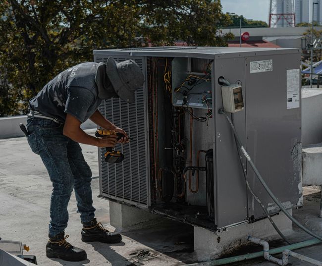 Worker servicing rooftop HVAC unit with open panel and exposed wiring
