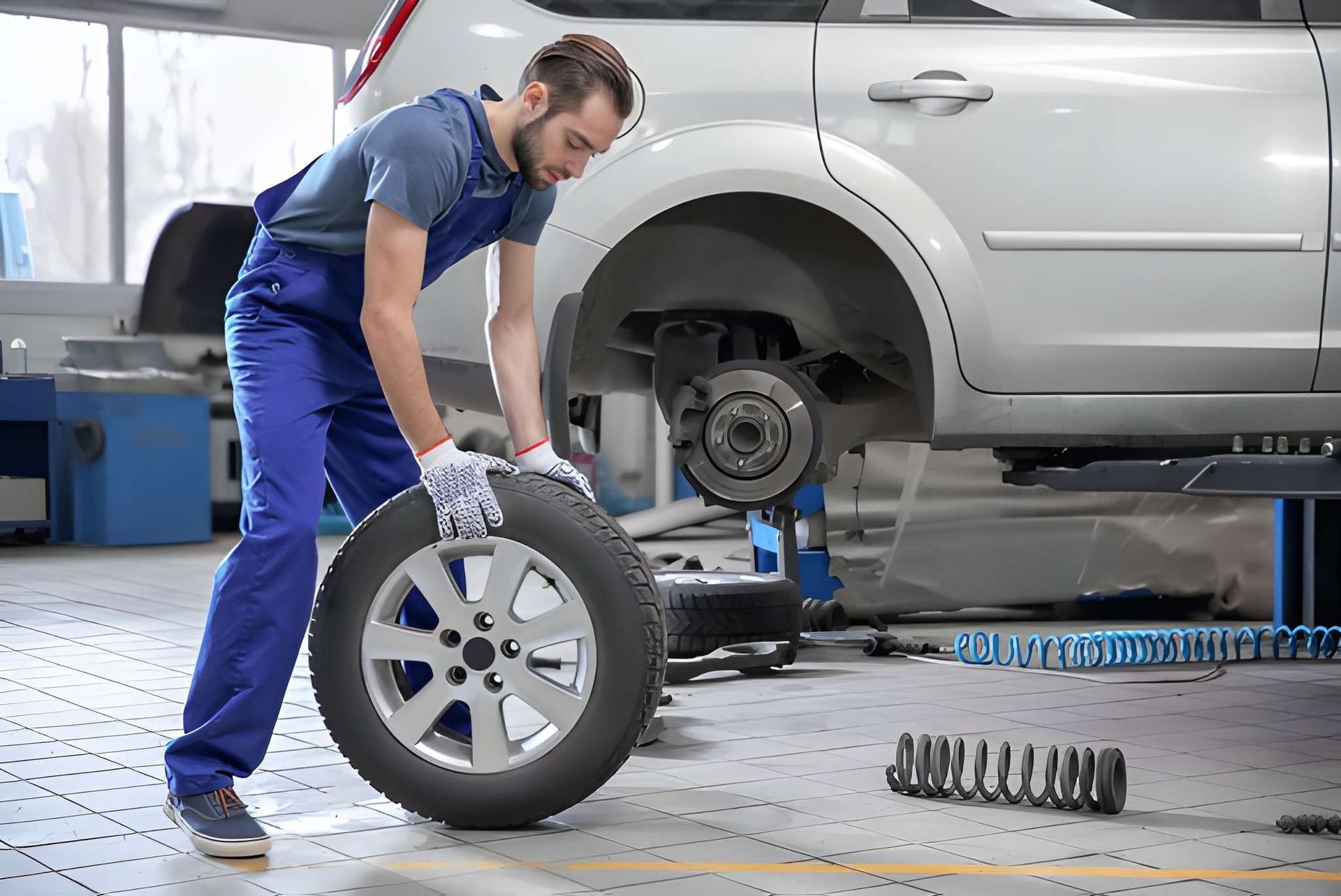 Mechanic in Blue Coveralls Changes a Car Tire in a Garage — Mechanical Care in Belconnen, ACT