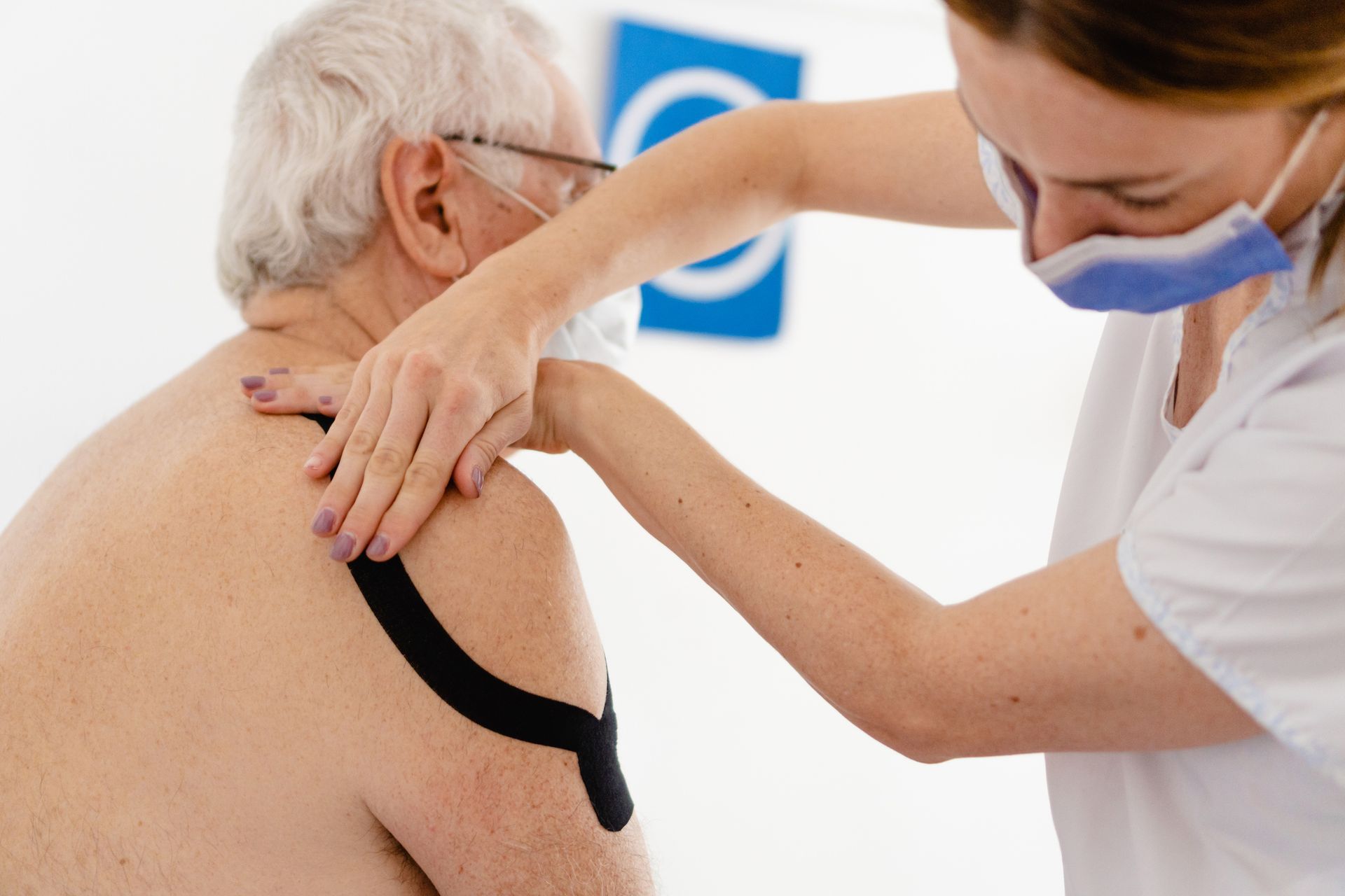 A nurse is applying kinesio tape to an older man 's shoulder.