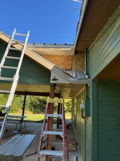 Two ladders leaning against a building with green siding and brown trim, under construction.