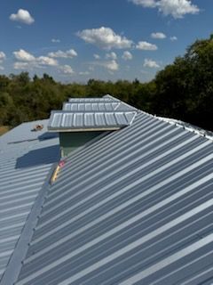 Metal roof with a corrugated pattern against a blue sky with clouds.