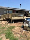 Wooden deck with stairs next to a house and pool; dirt yard in the foreground.