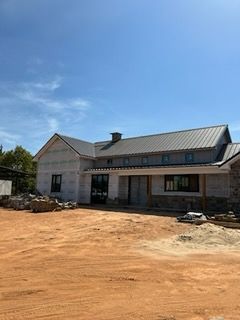 House under construction with stone and metal siding on a dirt lot.