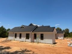 White house under construction with black metal roof and blue sky.