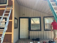 Exterior of a house with metal siding, door, windows, and ladders. Man in red shirt near ladder.