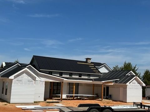 House under construction with black roof, white siding, and blue sky.
