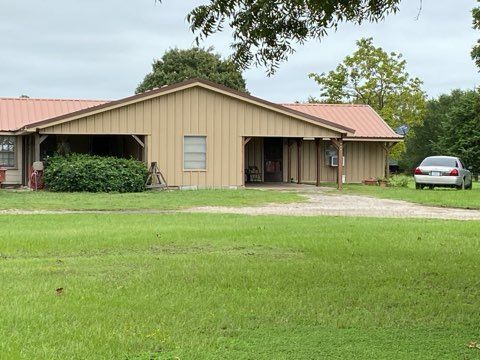 Tan house with red roof on green grass. A car is parked in the driveway. Overcast sky.