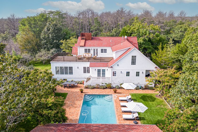 An aerial view of a large white house with a large swimming pool surrounded by trees.