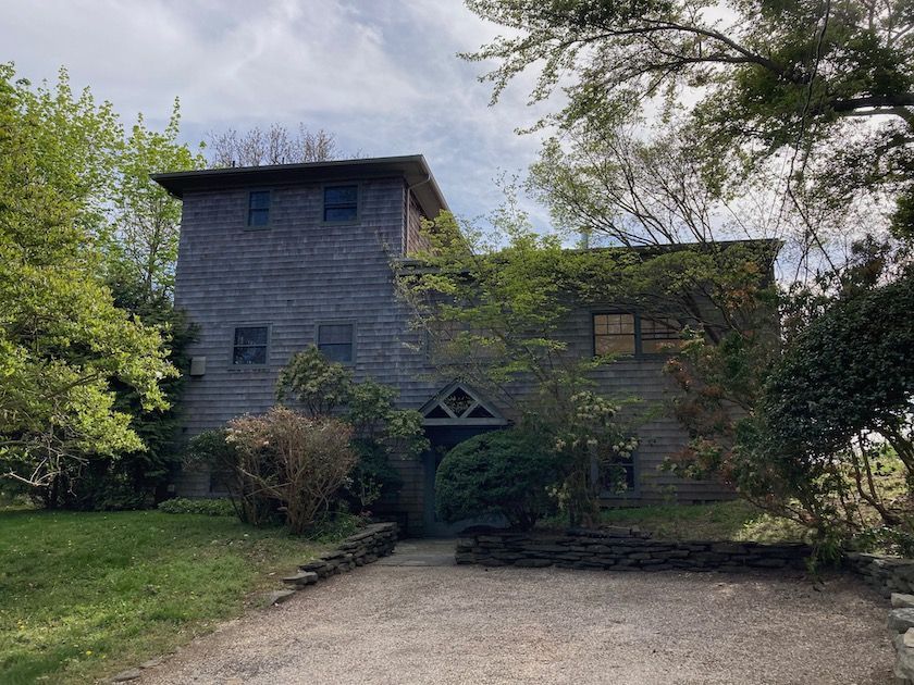 A large house with a gravel driveway leading to it is surrounded by trees.